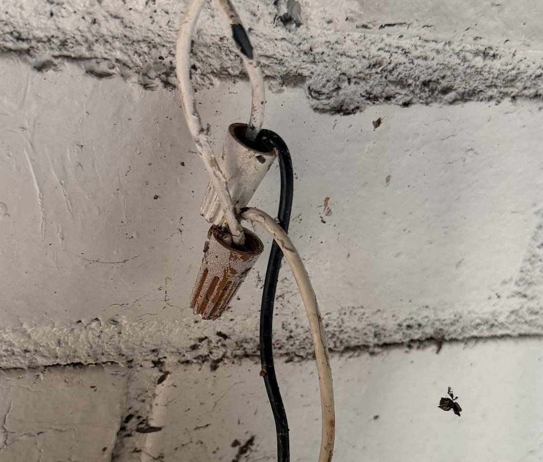 Close-up of two wire nuts hanging in open air on the brick wall, with cracked wire insulation